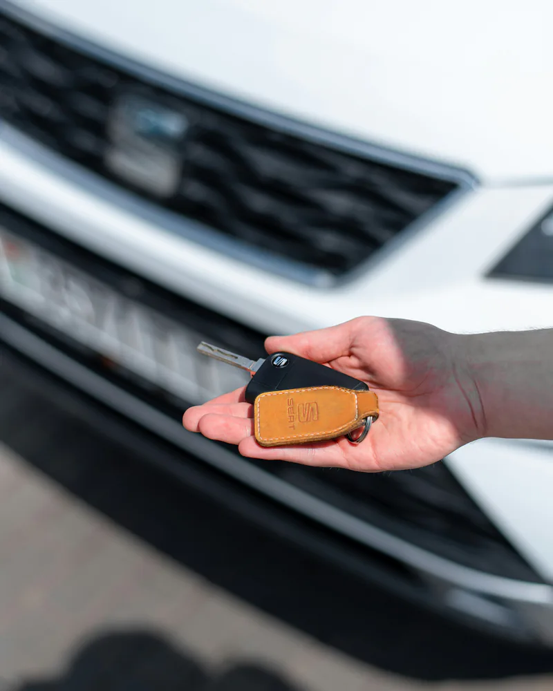 Hand übergibt einen Autoschlüssel vor einem Fahrzeug