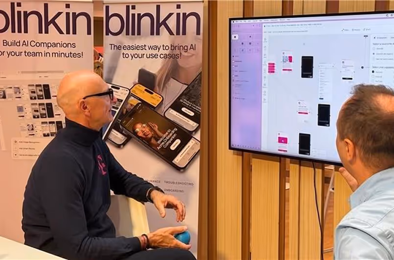 Two men looking at a large screen displaying a digital user interface design in a meeting room with BlinkIn AI promotional banners behind them.
